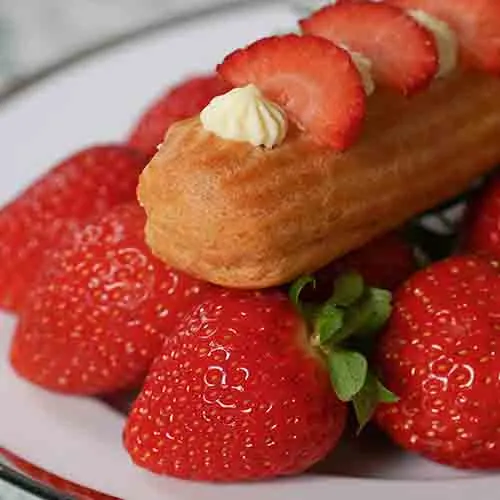 An eclair topped with cream and fresh strawberries, surrounded by strawberries