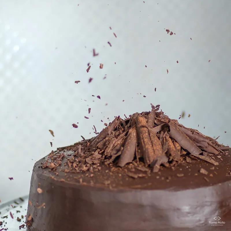 Chocolate shavings falling onto a chocolate cake piled with chocolate curls
